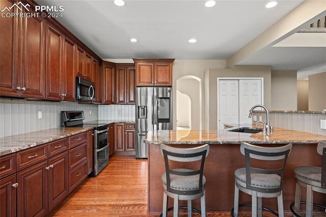 kitchen featuring light wood-type flooring, decorative backsplash, an island with sink, sink, and stainless steel appliances