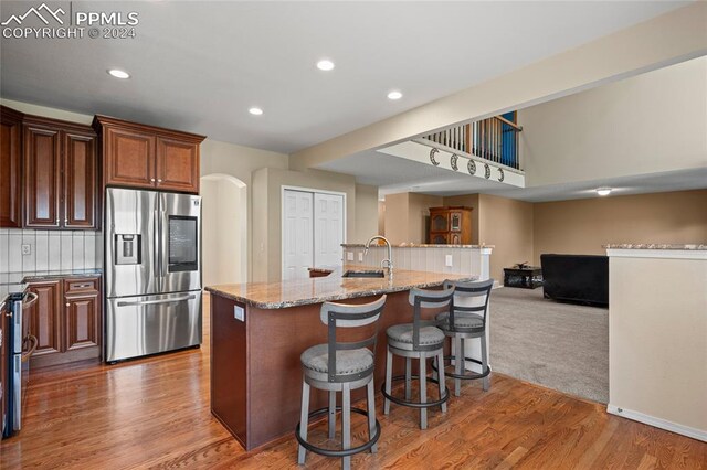 kitchen featuring carpet, tasteful backsplash, stainless steel refrigerator with ice dispenser, light stone counters, and a center island with sink