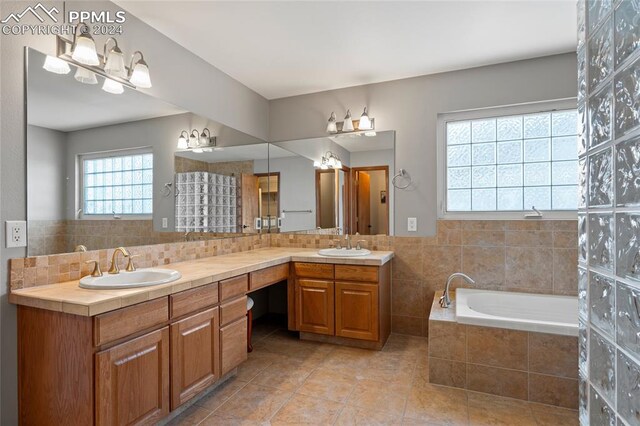 bathroom with tile patterned flooring, tiled tub, dual vanity, and tasteful backsplash