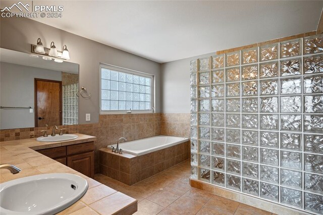 bathroom featuring tiled tub, dual vanity, and tile patterned floors