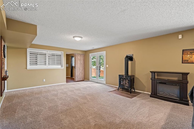 unfurnished living room featuring carpet flooring, a textured ceiling, and a wood stove