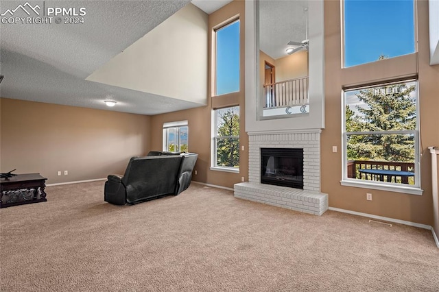 carpeted living room featuring a fireplace, ceiling fan, a high ceiling, and a textured ceiling