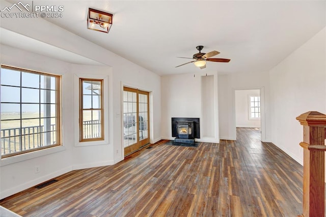 unfurnished living room featuring visible vents, baseboards, a wood stove, a ceiling fan, and wood finished floors