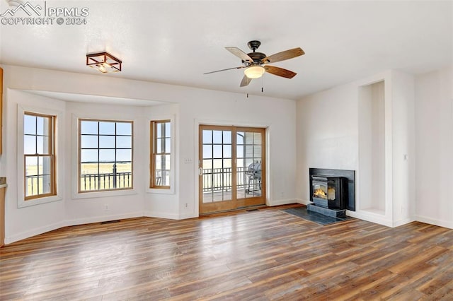 unfurnished living room with ceiling fan, wood-type flooring, a wealth of natural light, and a wood stove