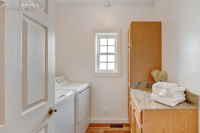 clothes washing area featuring light hardwood / wood-style floors, cabinets, and washer and clothes dryer