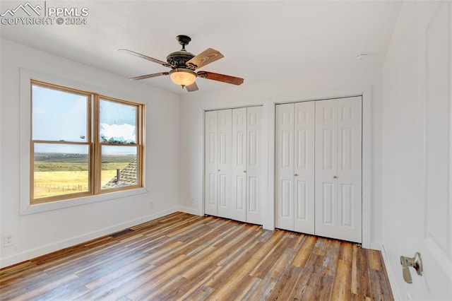 unfurnished bedroom with multiple closets, ceiling fan, and hardwood / wood-style floors