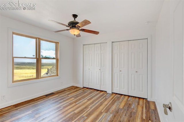 unfurnished bedroom with visible vents, multiple closets, wood finished floors, and baseboards