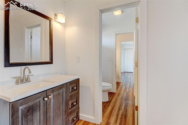 half bathroom with toilet, wood finished floors, vanity, and baseboards