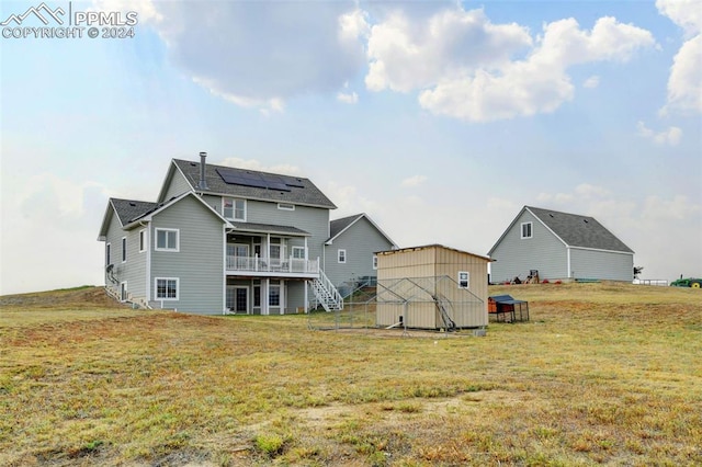 rear view of property featuring a storage shed, solar panels, a wooden deck, an outbuilding, and a lawn
