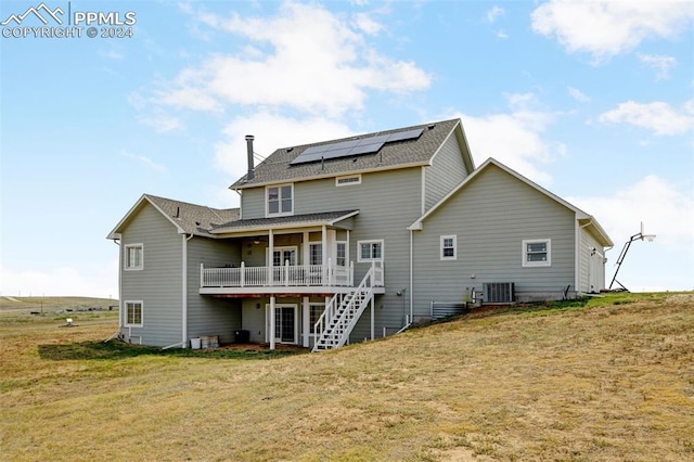 rear view of property with a deck, solar panels, a yard, stairs, and roof with shingles