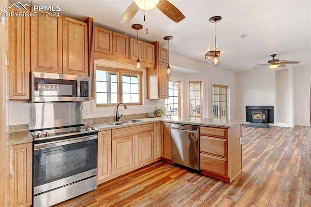 kitchen featuring stainless steel appliances, sink, kitchen peninsula, hanging light fixtures, and light hardwood / wood-style floors