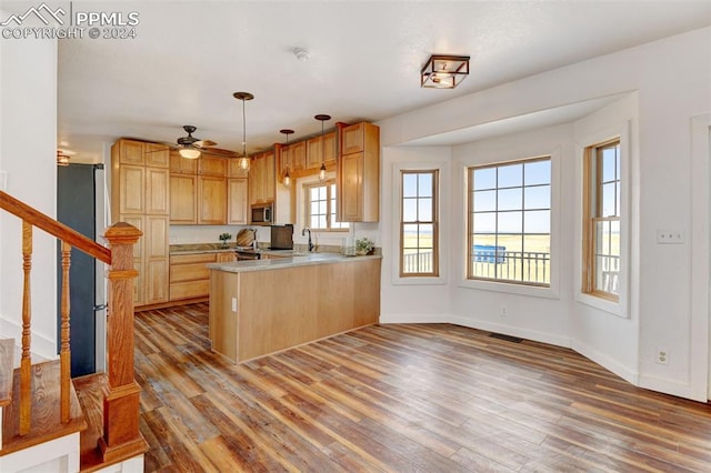 kitchen with light brown cabinets, kitchen peninsula, ceiling fan, hanging light fixtures, and hardwood / wood-style flooring