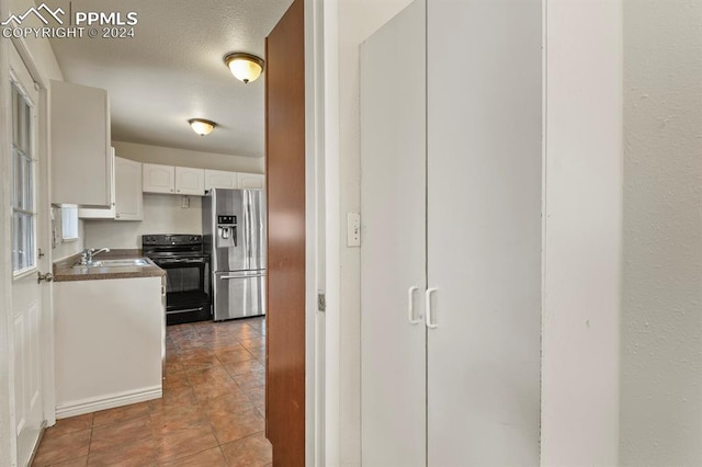 kitchen featuring stainless steel refrigerator with ice dispenser, white cabinets, tile patterned floors, sink, and stove