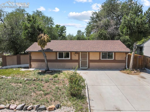 ranch-style home with a shingled roof, fence, and stucco siding