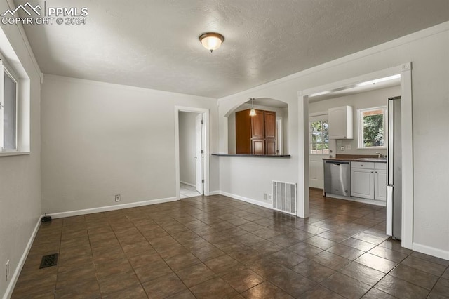 unfurnished living room featuring dark tile patterned flooring, sink, and a textured ceiling