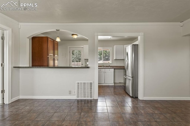 kitchen with sink, dark tile patterned flooring, stainless steel refrigerator, pendant lighting, and white cabinets