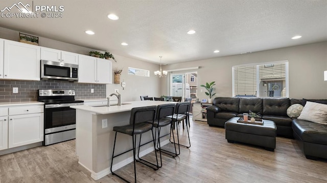 kitchen with appliances with stainless steel finishes, white cabinetry, a kitchen island with sink, and sink