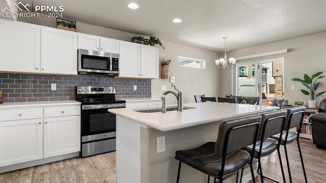 kitchen featuring a kitchen island with sink, white cabinets, sink, appliances with stainless steel finishes, and a notable chandelier