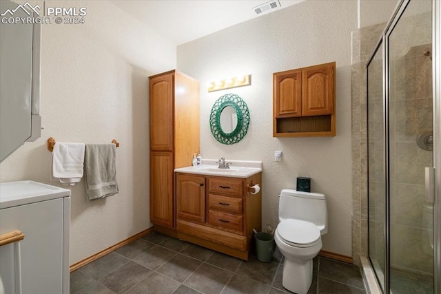 bathroom featuring stacked washer / drying machine, a shower with door, toilet, tile patterned floors, and vanity