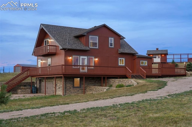 back house at dusk featuring a garage, a lawn, a balcony, and a deck