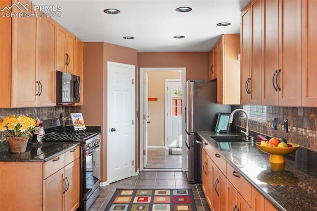 kitchen featuring sink, dark stone countertops, backsplash, dark tile patterned flooring, and range with gas cooktop