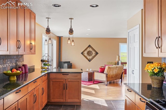 kitchen with decorative light fixtures, kitchen peninsula, dark tile patterned floors, decorative backsplash, and stove