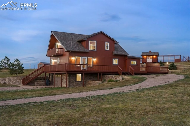 back house at dusk with a yard, a garage, a balcony, and a wooden deck