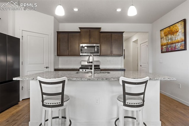 kitchen featuring hanging light fixtures, hardwood / wood-style floors, a center island with sink, and stainless steel appliances