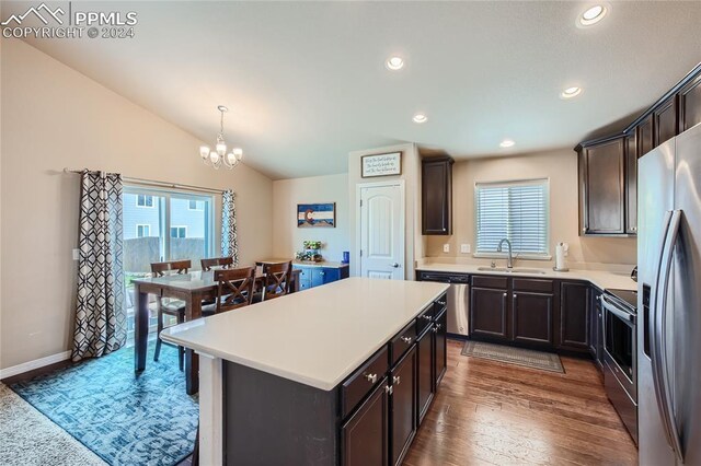 kitchen featuring stainless steel appliances, decorative light fixtures, a kitchen island, sink, and lofted ceiling