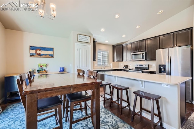 kitchen featuring vaulted ceiling, a kitchen breakfast bar, stainless steel appliances, a chandelier, and dark brown cabinetry