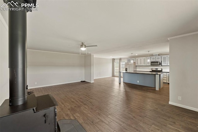 unfurnished living room with ceiling fan, dark hardwood / wood-style flooring, ornamental molding, and a wood stove