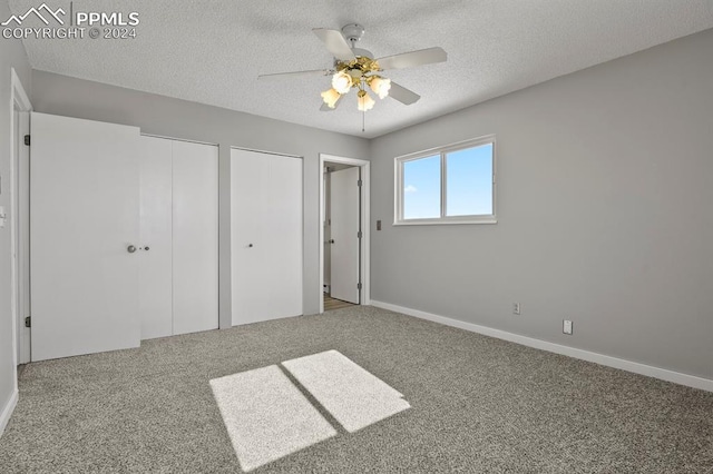 unfurnished bedroom featuring ceiling fan, a textured ceiling, carpet flooring, and multiple closets