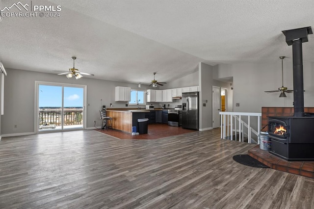 kitchen featuring stainless steel appliances, a wood stove, lofted ceiling, white cabinets, and dark wood-type flooring