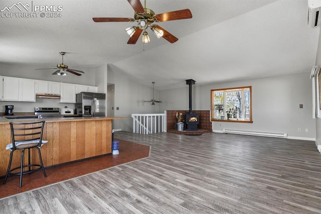 kitchen with appliances with stainless steel finishes, a kitchen bar, vaulted ceiling, hardwood / wood-style flooring, and baseboard heating