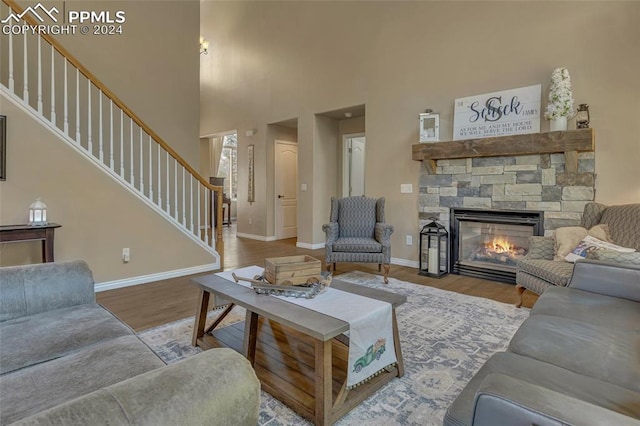 living room featuring a stone fireplace, a high ceiling, and hardwood / wood-style flooring