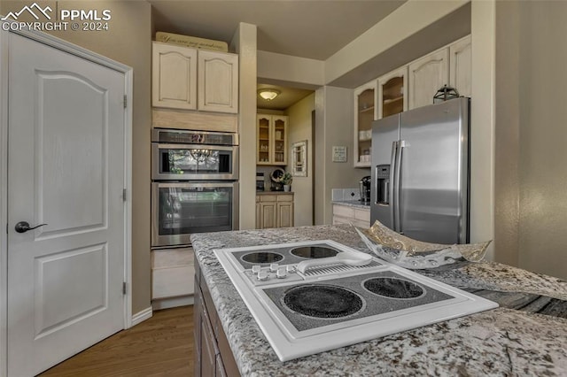 kitchen with cream cabinetry, hardwood / wood-style floors, stainless steel appliances, and light stone countertops