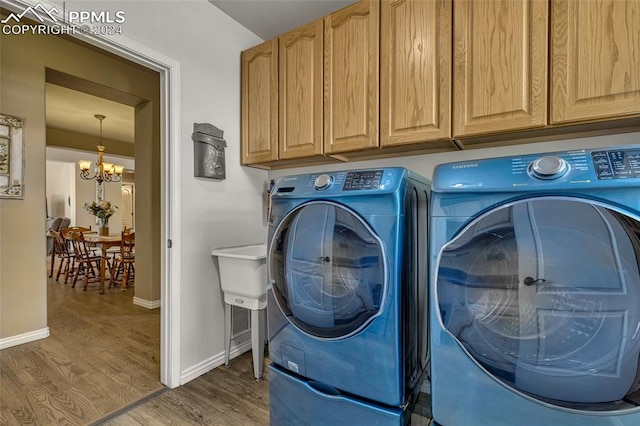 washroom featuring cabinets, hardwood / wood-style floors, washing machine and dryer, and a chandelier