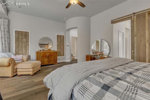 bedroom featuring hardwood / wood-style flooring, ceiling fan, and a barn door