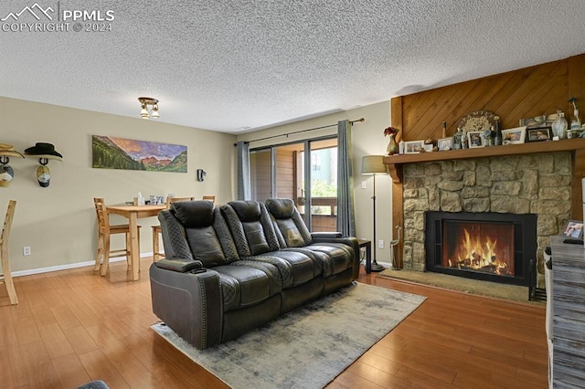 living room featuring wooden walls, wood-type flooring, a stone fireplace, and a textured ceiling