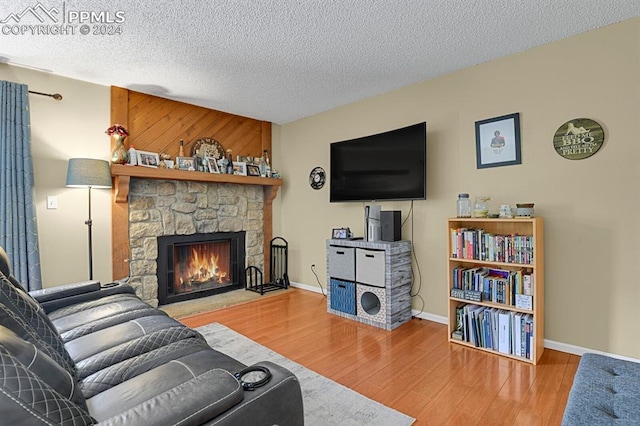 living room with a stone fireplace, a textured ceiling, and hardwood / wood-style flooring