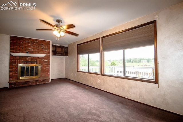 unfurnished living room with dark colored carpet, ceiling fan, brick wall, and a brick fireplace