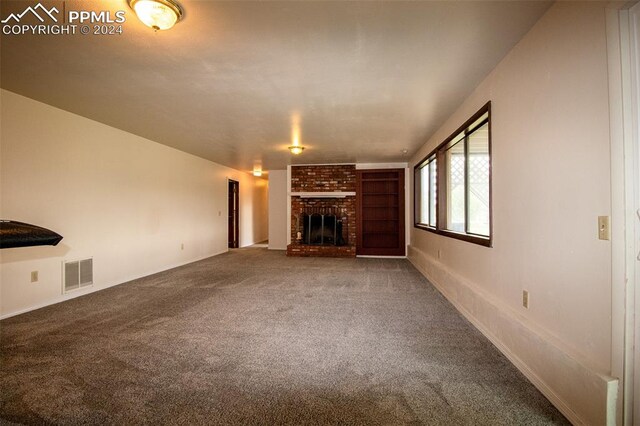 unfurnished living room with a fireplace, brick wall, and carpet