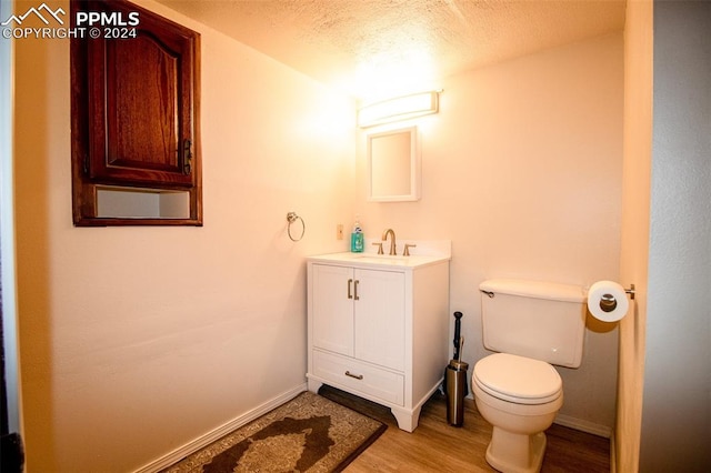 bathroom with a textured ceiling, wood-type flooring, vanity, and toilet