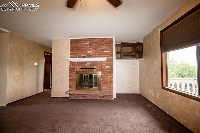 unfurnished living room with a brick fireplace, dark carpet, and ceiling fan