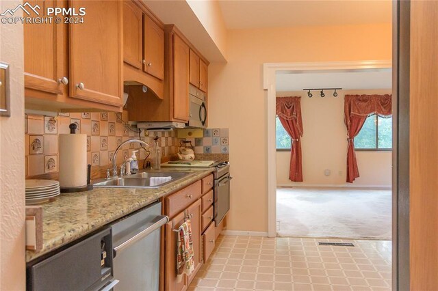 kitchen featuring rail lighting, sink, light carpet, stainless steel appliances, and decorative backsplash