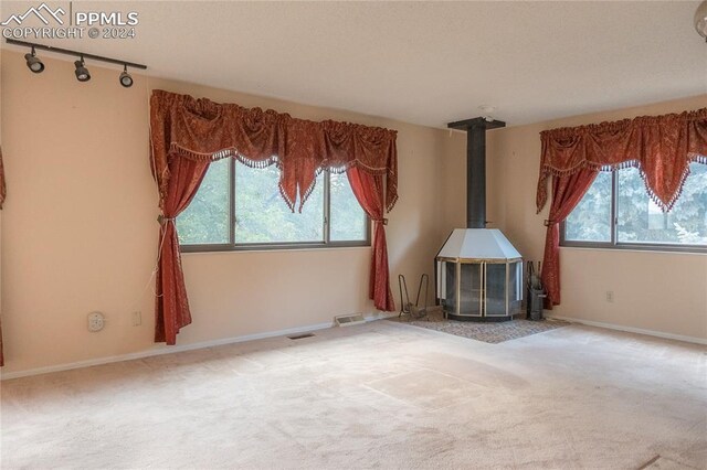 unfurnished living room featuring carpet floors, a wealth of natural light, track lighting, and a wood stove