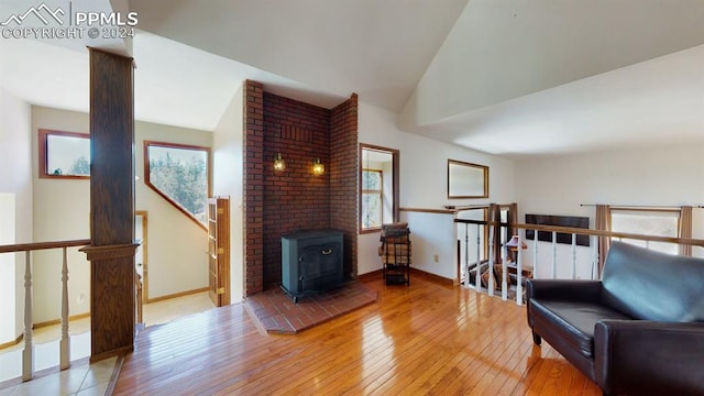 living area featuring a wood stove, brick wall, hardwood / wood-style floors, and vaulted ceiling