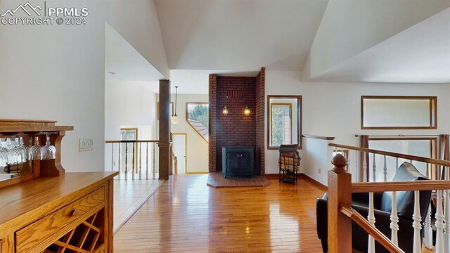 interior space featuring brick wall, light wood-type flooring, a wood stove, and high vaulted ceiling