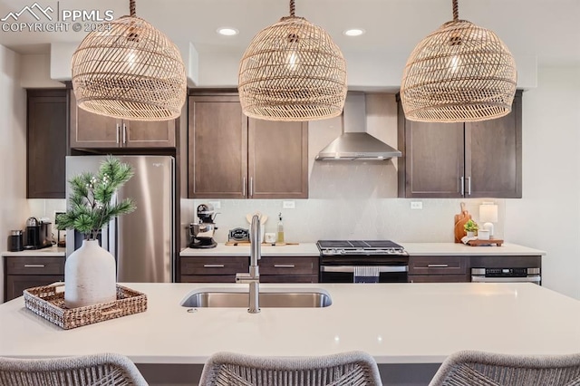 kitchen with dark brown cabinetry, pendant lighting, sink, wall chimney range hood, and stainless steel appliances