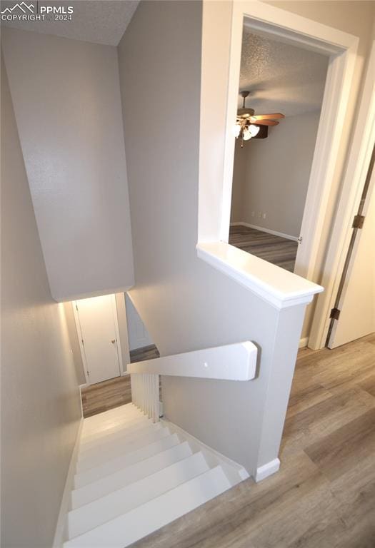 stairs featuring a textured ceiling, wood-type flooring, and ceiling fan